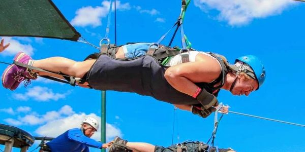 Person ziplining horizontally with safety gear against a blue sky.