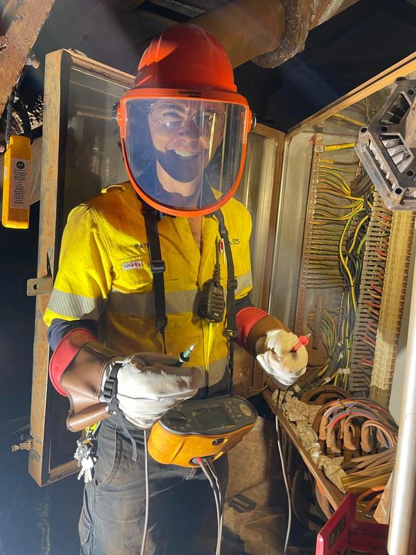 Electrician in safety gear inspecting electrical panel with testing device.