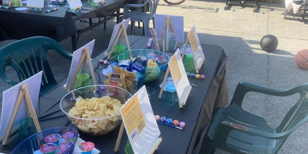 Outdoor painting setup with snacks and miniature easels on tables.