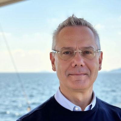 Man with glasses standing in front of a body of water.