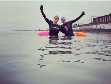 Two female swimmers in the sea, wearing wetsuits and smiling