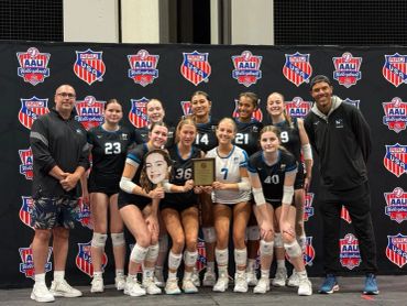 Girls volleyball team celebrating with trophy.