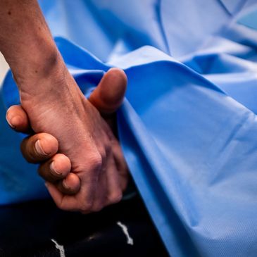 Two people holding hands, one covered by a blue medical sheet.