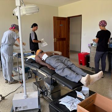 Patient lies on medical table surrounded by three healthcare workers in a clinical room.