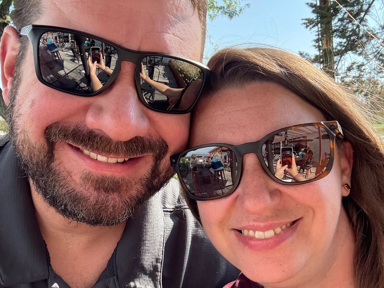 Smiling couple wearing sunglasses outdoors on a sunny day.