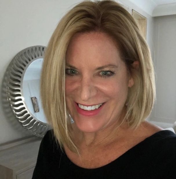 Smiling woman with blonde hair and a black top indoors.