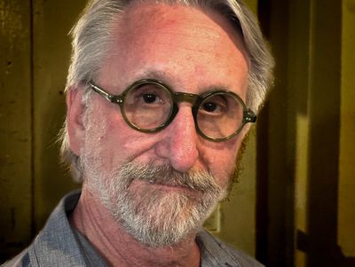 Close-up of an elderly man with round glasses and a beard.