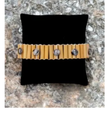 Beige bracelet with silver skulls displayed on a black cushion.