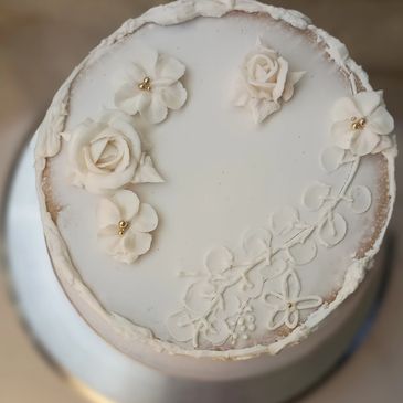 Elegant white cake decorated with delicate white flowers and gold beads.