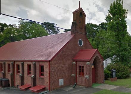 A small brick church with a red metal roof and steeple.
