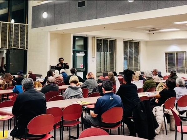 Community meeting with people listening to a speaker in a large room.