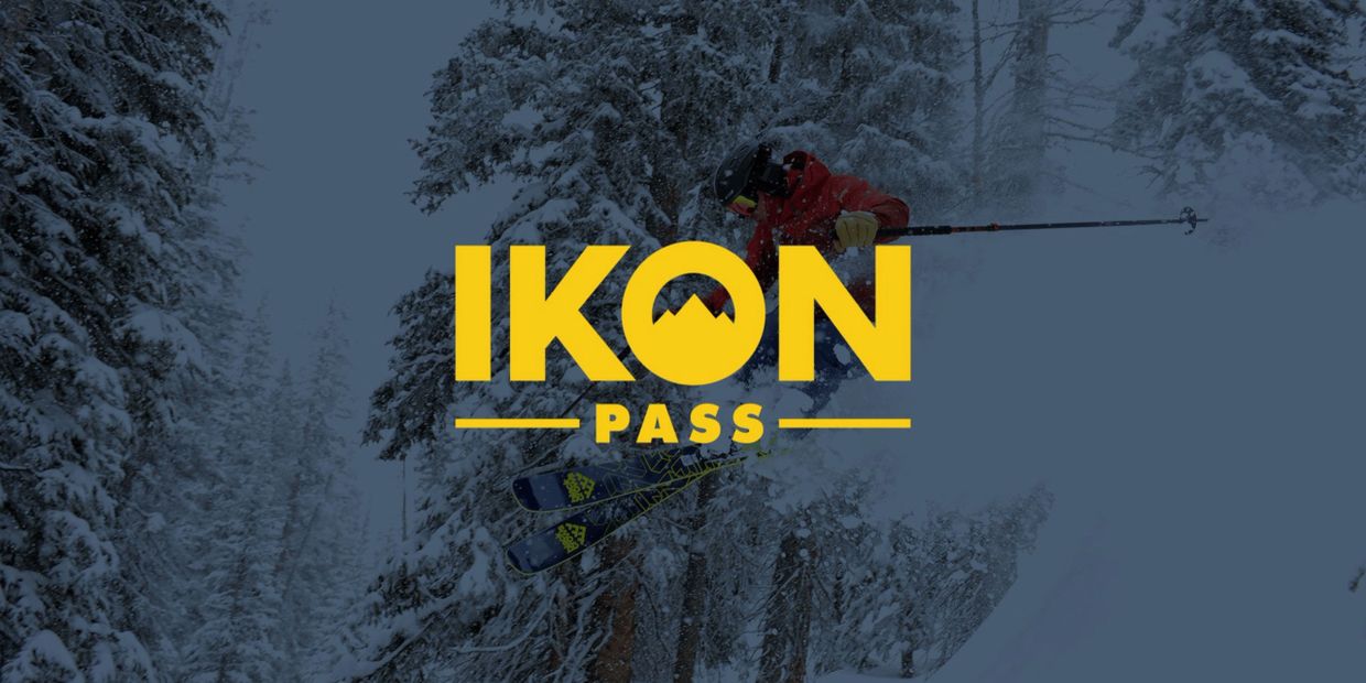 Skier performing a jump in snowy forest with IKON Pass logo.