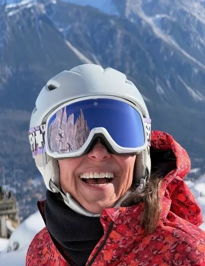 Smiling skier wearing a helmet and reflective goggles with mountain reflection.