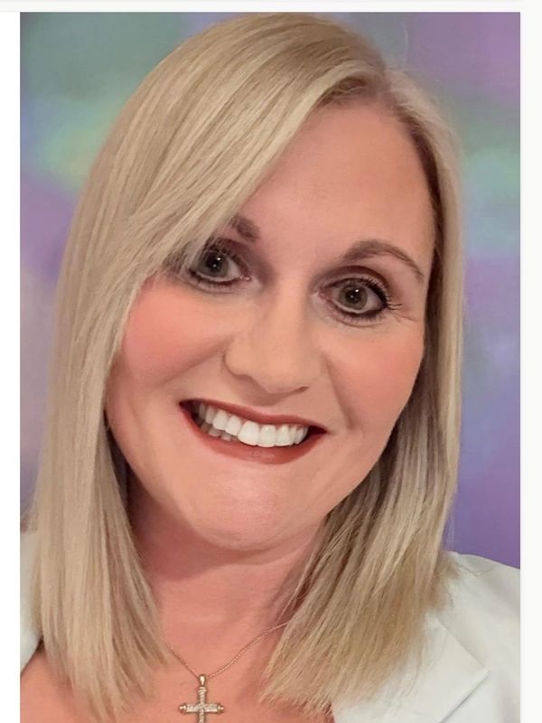 Smiling woman with blonde hair and cross necklace.