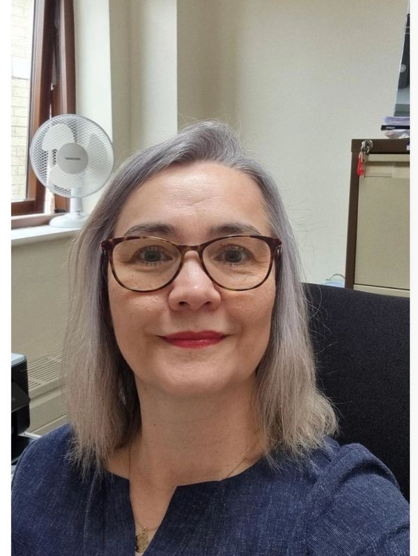 Woman with glasses smiling indoors near a window.