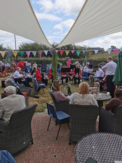 Outdoor gathering with live band and seated audience under shade sails.