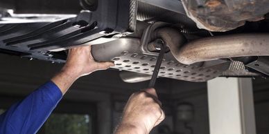 Mechanic tightening bolts under a car's exhaust system with a wrench.