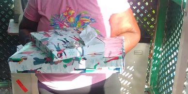 Person holding wrapped gifts on a porch with sunlight.