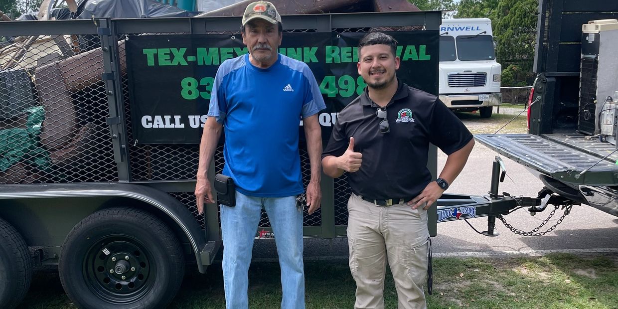 Two men standing in front of a trailer loaded with furniture and debris on a sunny day.