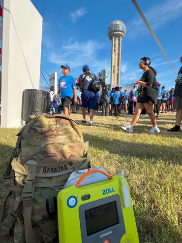 Crowd gathered near Reunion Tower with a medical backpack and ZOLL defibrillator in the foreground.