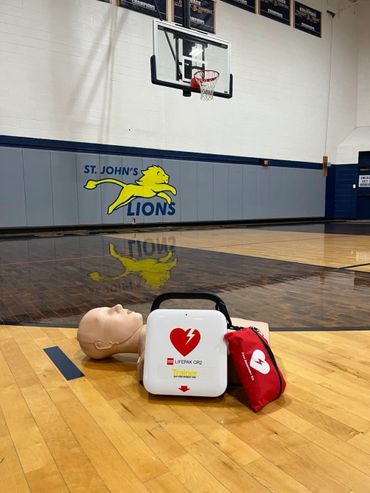 CPR training setup with a mannequin and defibrillator on a basketball court.