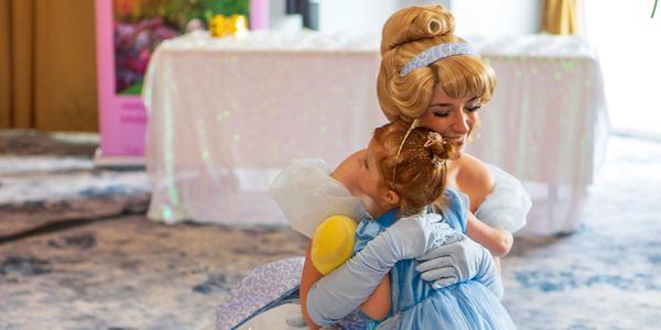 A princess warmly hugging a young girl dressed as Cinderella.