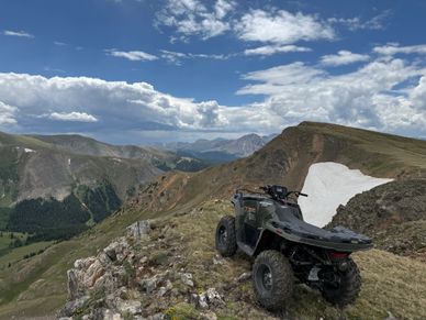 An ATV parked on a mountain ridge under a partly cloudy sky.