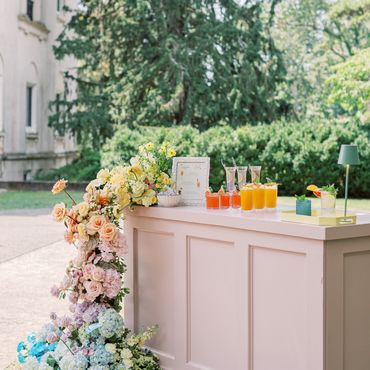 Outdoor pastel pink bar decorated with colorful flowers and refreshing drinks.
