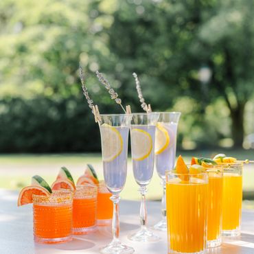 Assorted colorful cocktails garnished with fruits and herbs on a sunny table.