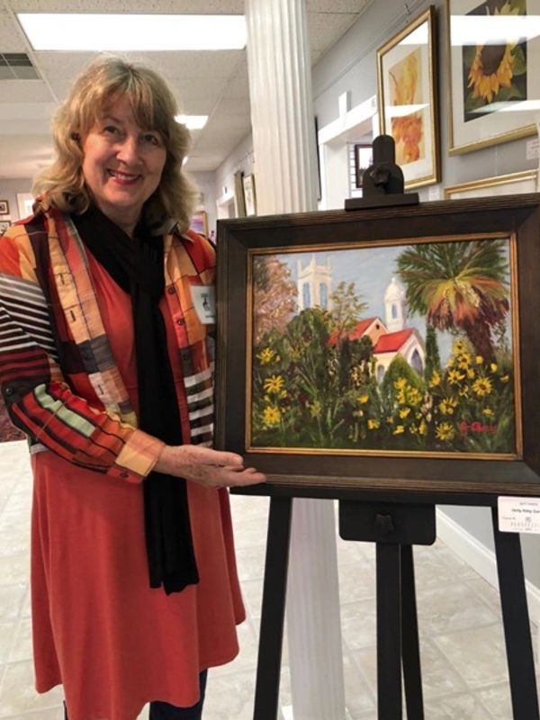 Woman proudly displaying a framed floral landscape painting on an easel.