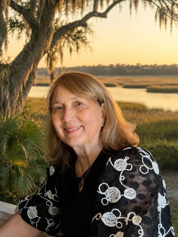 Smiling woman with blonde hair in a scenic outdoor setting at sunset.