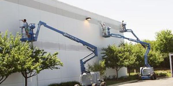 Workers using boom lifts to paint a large exterior wall.