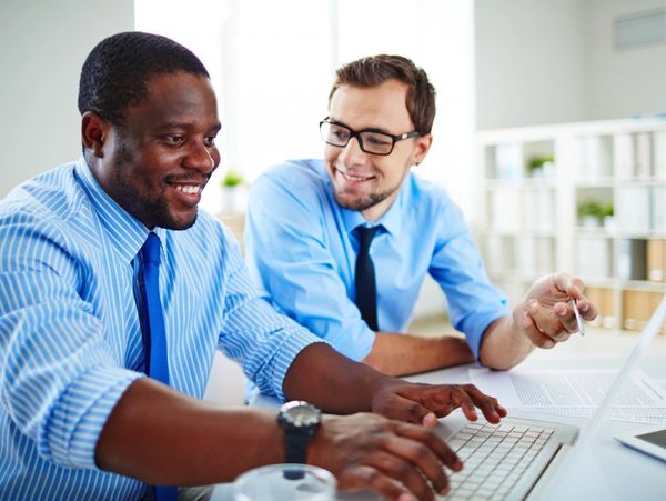 Two professionals collaborate at a laptop, discussing documents on a bright office