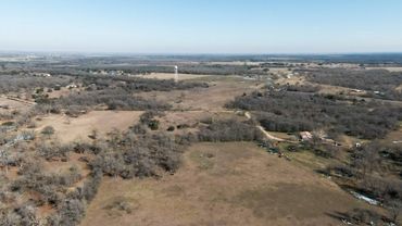 A vast rural landscape with sparse trees and a water tower under clear skies.