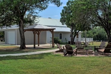 Outdoor seating area with wooden chairs around a fire pit near a modern building.