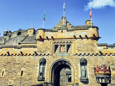 Historic stone castle entrance under a clear blue sky with flags.