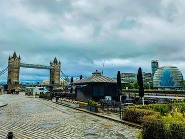 View of Tower Bridge and surrounding riverside buildings in London under a cloudy sky.