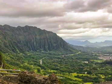 Panoramic view of lush green valley and rugged mountains under a cloudy sky.