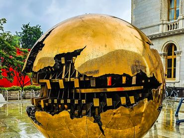 A large golden spherical sculpture with intricate cutouts outdoors.