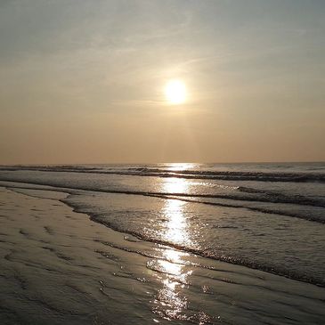 Calm beach scene with the sun reflecting on wet sand and gentle waves.