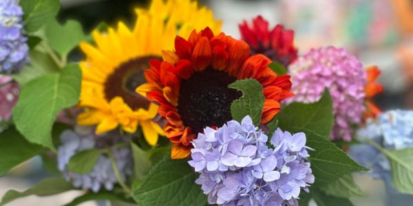 A vibrant bouquet featuring sunflowers, hydrangeas, and lush green leaves.