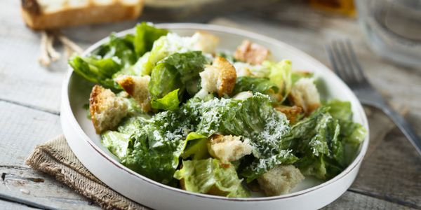 Fresh Caesar salad with lettuce, croutons, and grated cheese in a white bowl.