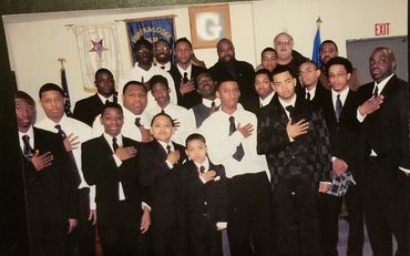Group of men and boys in suits posing with hand-over-heart gesture indoors.