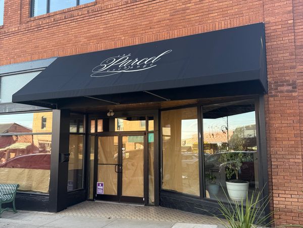 Black awning with the name "Eli'sica" above glass doors on a brick building.