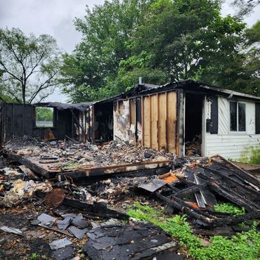 A house severely damaged by fire with charred remains scattered around.