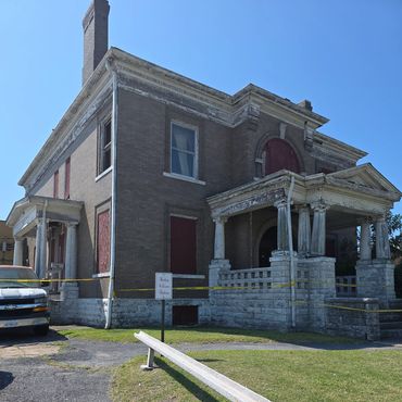 Old abandoned brick house with boarded windows and caution tape.