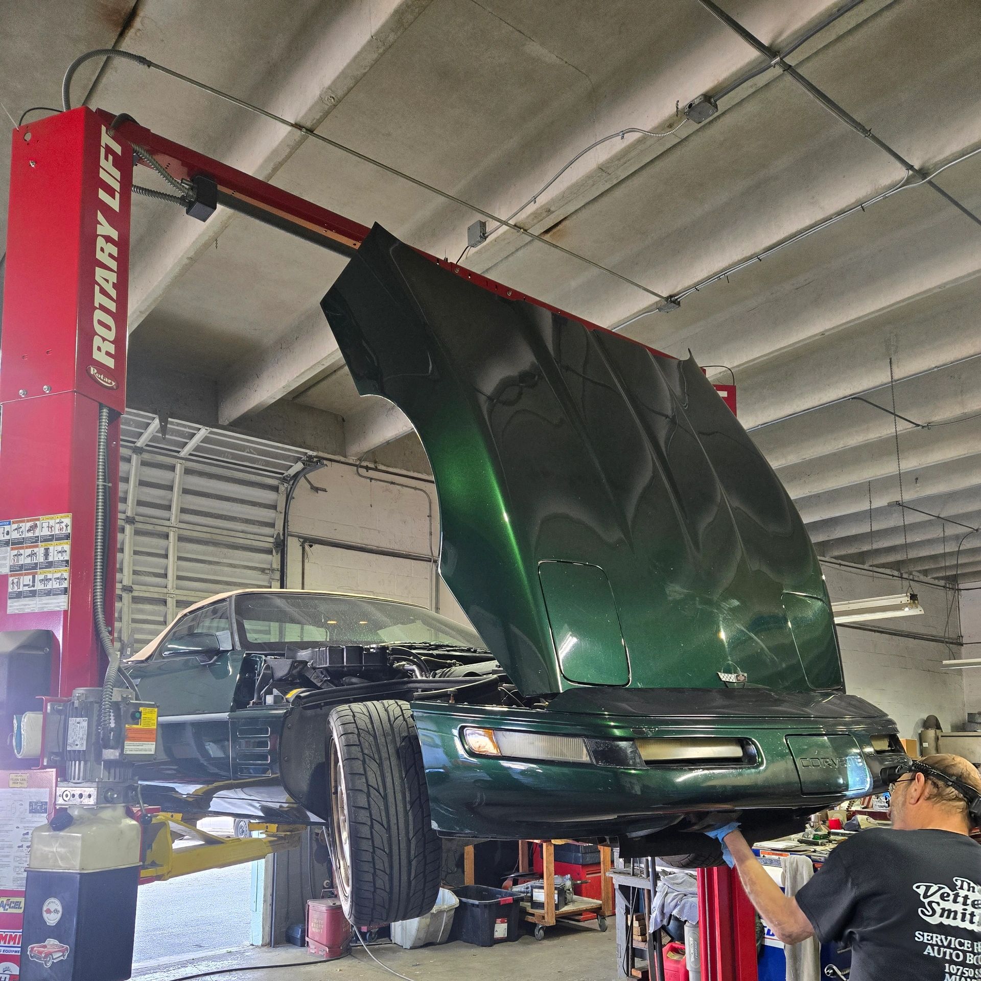 Green Corvette raised on a rotary lift with hood open.