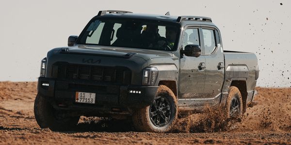 A black Kia pickup truck driving fast on muddy terrain.