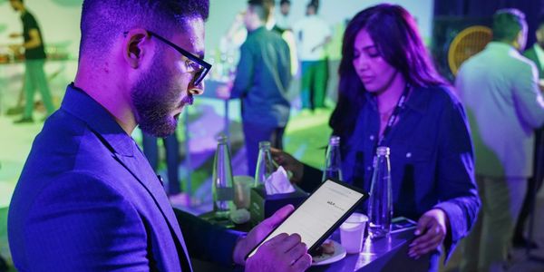 Man using a tablet at a social event with people in the background.