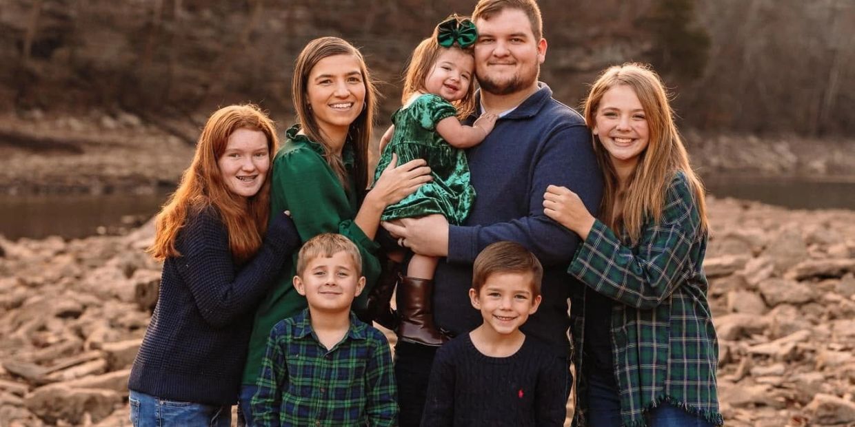 A happy family of seven posing outdoors on rocky terrain in warm clothing.